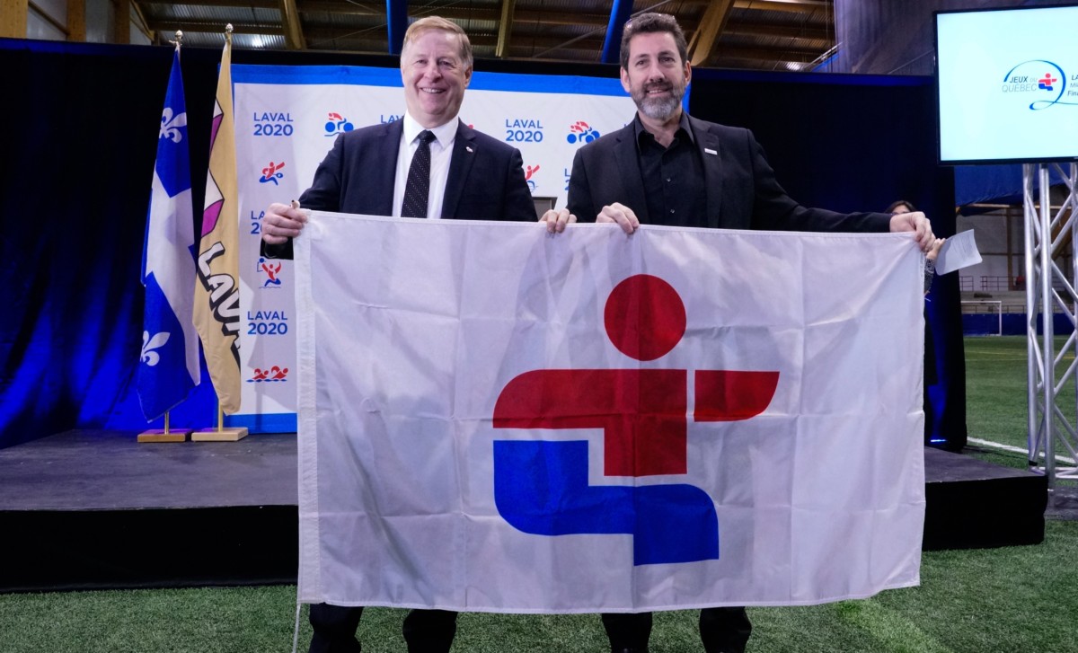 Marc Demers tient fièrement le drapeau des Jeux du Québec que lui remet Michel Allen, de SPORTSQUÉBEC.